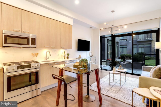 kitchen with light hardwood / wood-style floors, light brown cabinetry, appliances with stainless steel finishes, and a chandelier