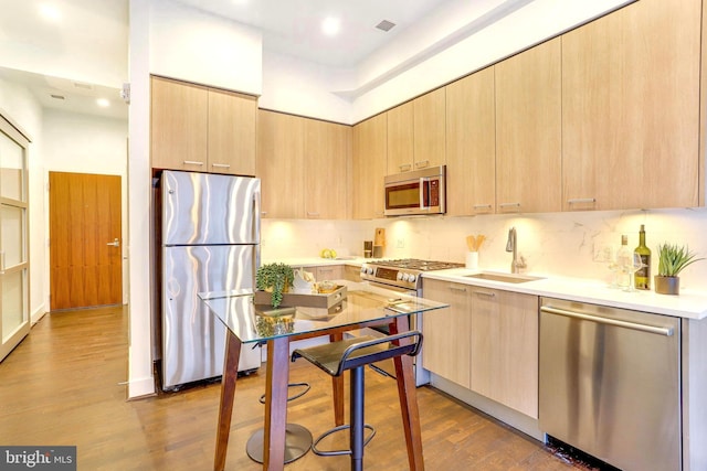 kitchen featuring sink, wood-type flooring, stainless steel appliances, and light brown cabinetry