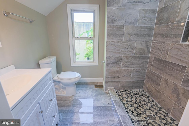 bathroom with tiled shower, vanity, vaulted ceiling, and toilet