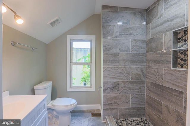 bathroom featuring toilet, vanity, tiled shower, and vaulted ceiling