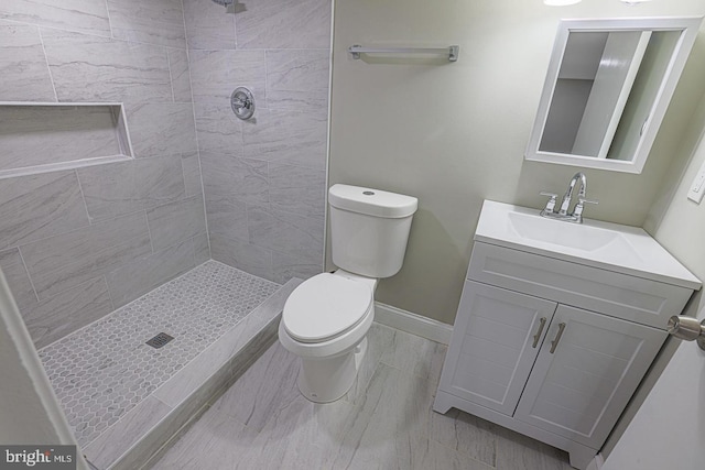 bathroom featuring a tile shower, vanity, and toilet