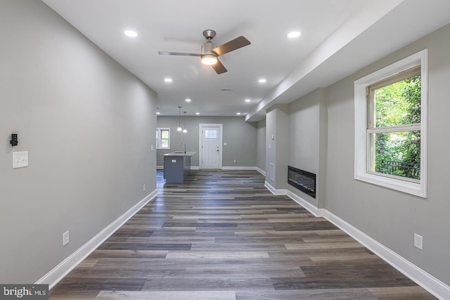 unfurnished living room with ceiling fan, sink, and dark wood-type flooring