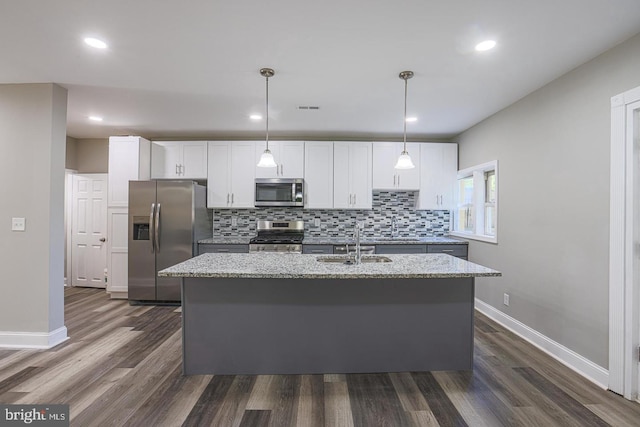 kitchen featuring appliances with stainless steel finishes, a center island with sink, light stone counters, and pendant lighting