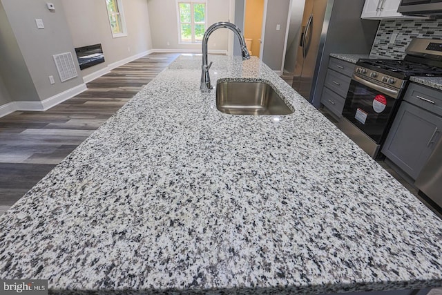 kitchen with a center island with sink, light stone counters, stainless steel gas range oven, and sink