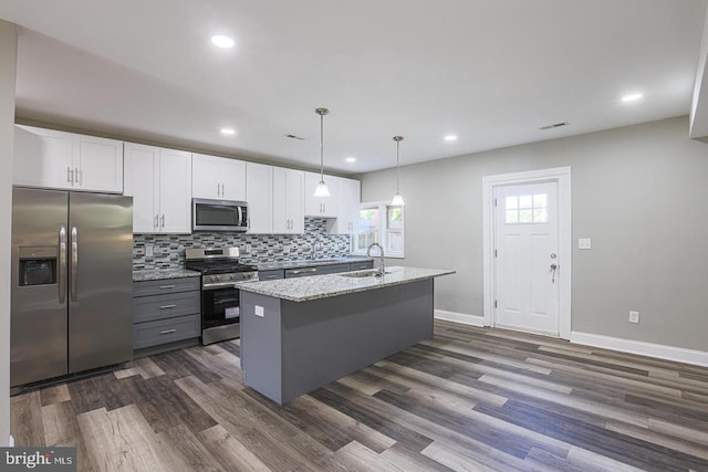 kitchen with white cabinets, decorative light fixtures, stainless steel appliances, and a kitchen island with sink