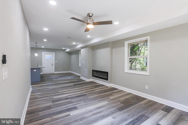 unfurnished living room featuring ceiling fan, sink, and dark wood-type flooring