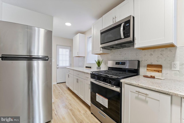 kitchen featuring light hardwood / wood-style flooring, appliances with stainless steel finishes, tasteful backsplash, light stone counters, and white cabinetry