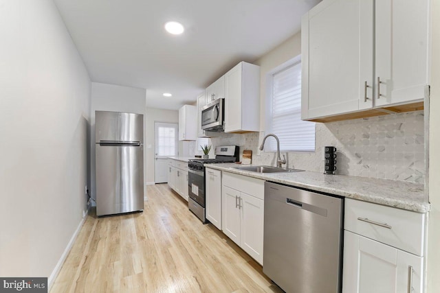 kitchen with appliances with stainless steel finishes, backsplash, sink, light hardwood / wood-style floors, and white cabinetry