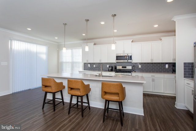 kitchen with a kitchen island with sink, hanging light fixtures, white cabinetry, stainless steel appliances, and a kitchen breakfast bar