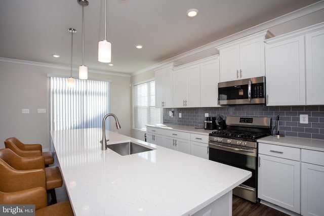 kitchen featuring appliances with stainless steel finishes, white cabinetry, sink, hanging light fixtures, and a center island with sink