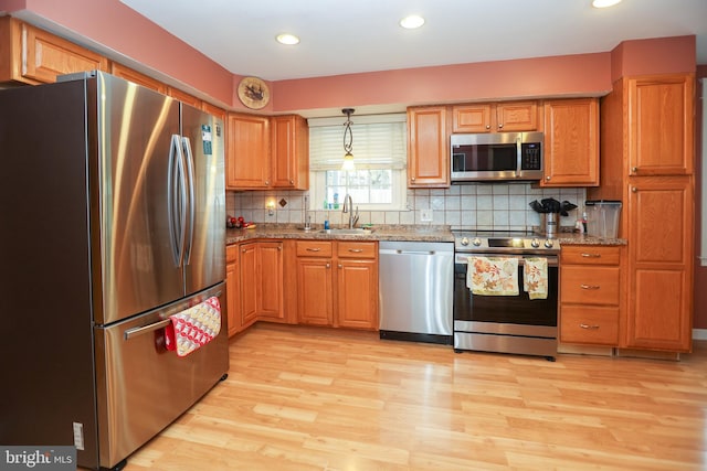 kitchen with sink, hanging light fixtures, light hardwood / wood-style floors, decorative backsplash, and appliances with stainless steel finishes