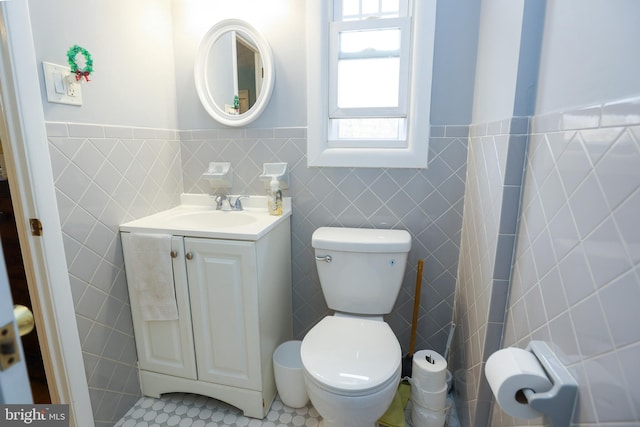 bathroom with toilet, vanity, tile patterned floors, and tile walls