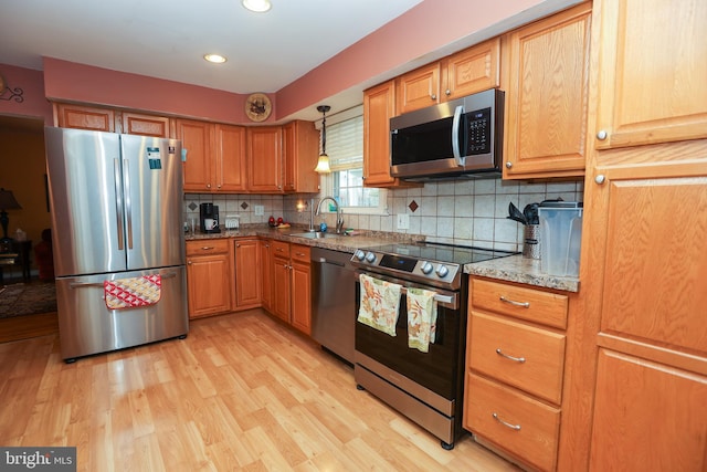 kitchen with sink, light wood-type flooring, appliances with stainless steel finishes, tasteful backsplash, and stone countertops