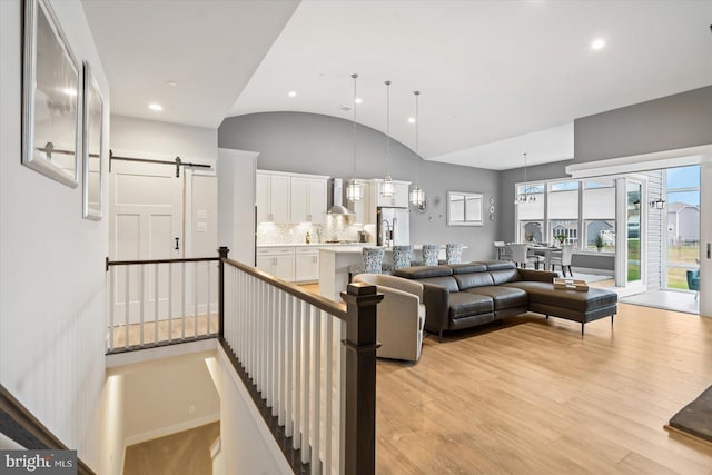 living room featuring a barn door, high vaulted ceiling, and light hardwood / wood-style flooring