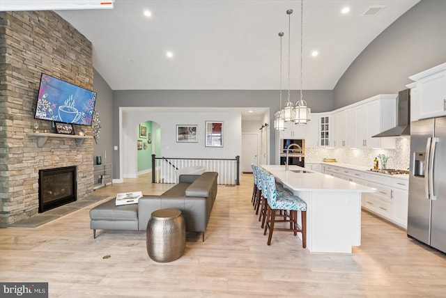 kitchen featuring stainless steel appliances, white cabinetry, a center island with sink, and wall chimney range hood