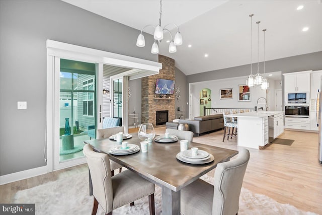 dining room with sink, a fireplace, vaulted ceiling, and light wood-type flooring