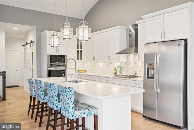 kitchen featuring appliances with stainless steel finishes, wall chimney exhaust hood, sink, a barn door, and white cabinets