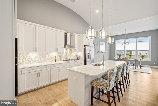 kitchen with white cabinets, wall chimney range hood, sink, an island with sink, and stainless steel appliances