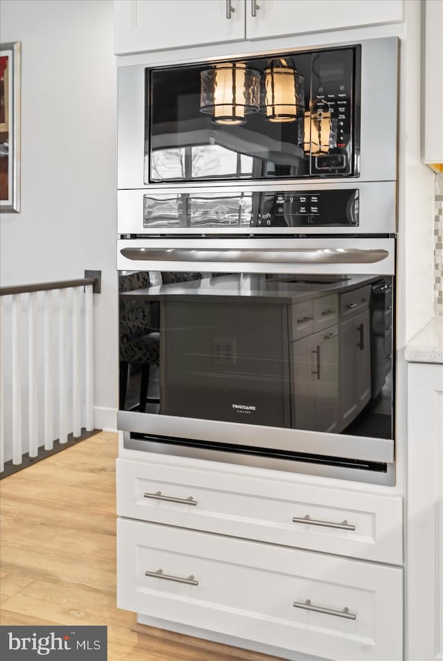 kitchen featuring light wood-type flooring, white cabinetry, built in microwave, and light stone counters