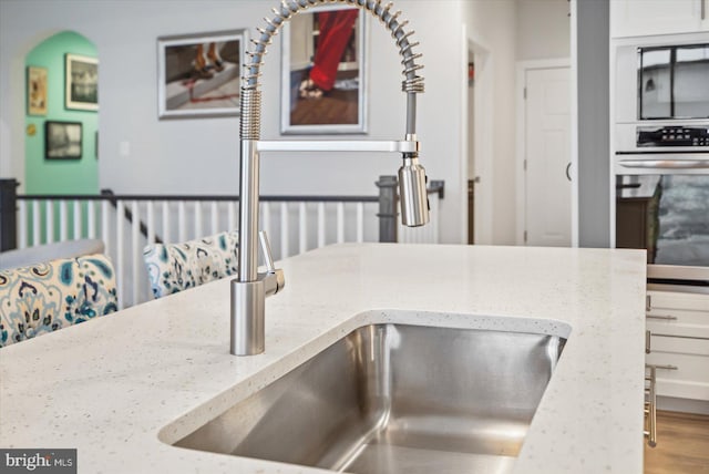 details with white cabinetry, light stone counters, stainless steel oven, and sink