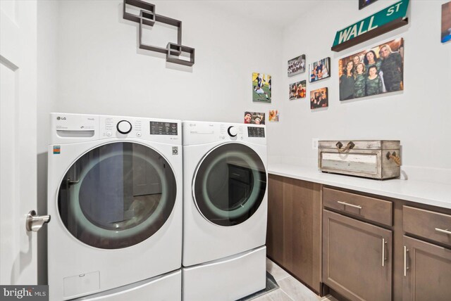 washroom featuring washer and clothes dryer, light tile patterned flooring, and cabinets