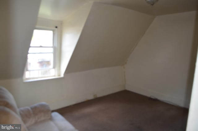 additional living space with dark colored carpet and vaulted ceiling