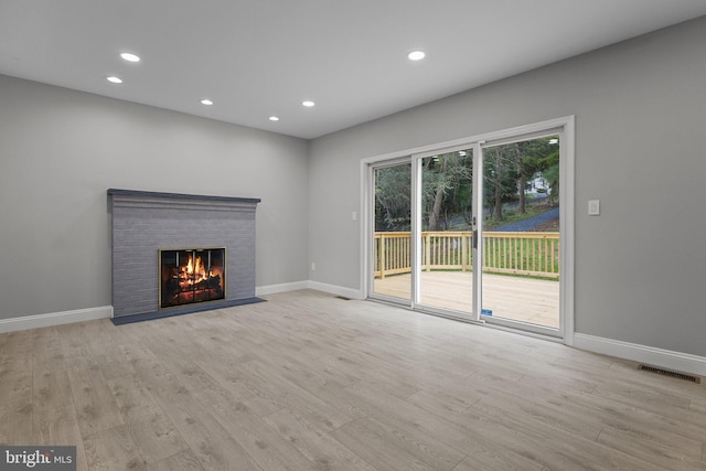 unfurnished living room featuring light hardwood / wood-style floors and a brick fireplace