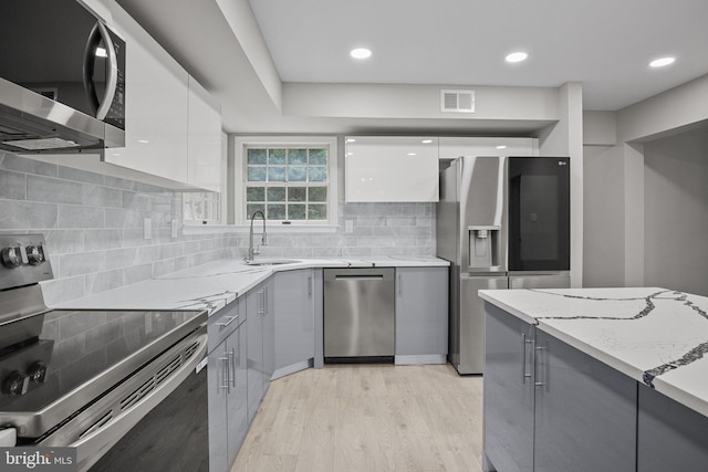 kitchen with white cabinetry, appliances with stainless steel finishes, sink, and light stone counters