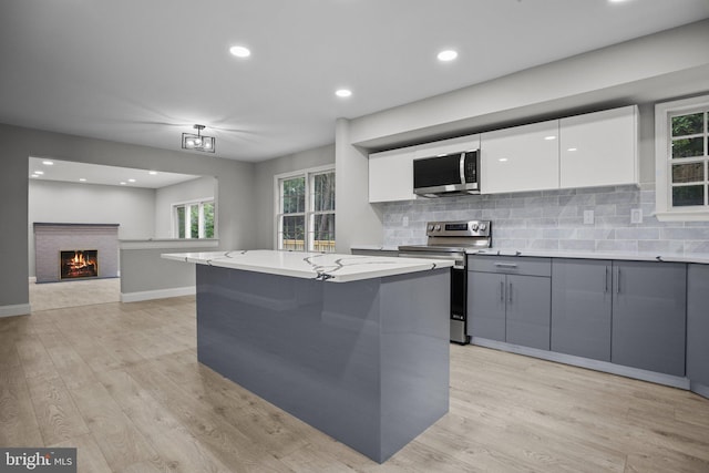 kitchen with gray cabinetry, stainless steel appliances, light stone counters, white cabinets, and a kitchen island