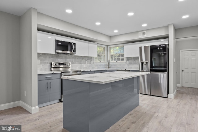 kitchen with white cabinetry, stainless steel appliances, a kitchen island, and light hardwood / wood-style flooring