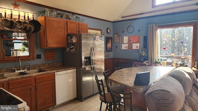 kitchen with lofted ceiling, white dishwasher, sink, wooden walls, and stainless steel fridge