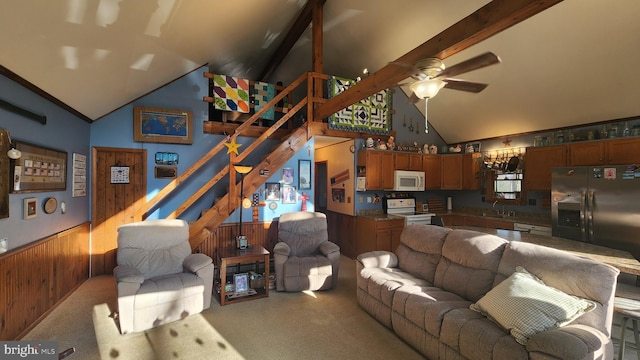 carpeted living room with wooden walls, beamed ceiling, ceiling fan, and high vaulted ceiling