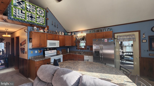 kitchen with pendant lighting, white appliances, wood walls, and sink