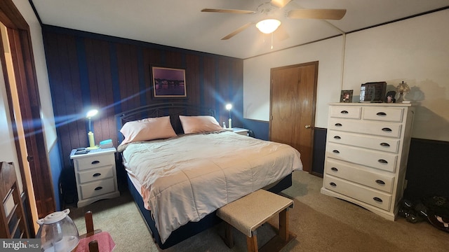 carpeted bedroom with ceiling fan and wood walls