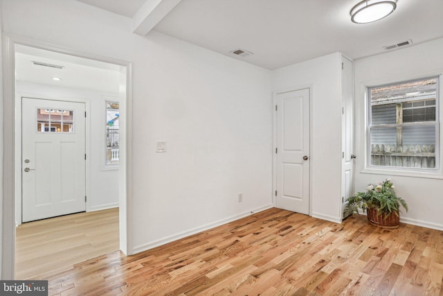 empty room with light hardwood / wood-style floors, beam ceiling, and a wealth of natural light