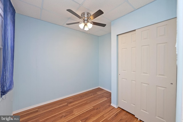 unfurnished bedroom featuring hardwood / wood-style floors, ceiling fan, a drop ceiling, and a closet