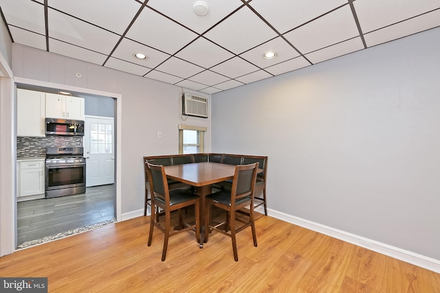 dining room with a wall mounted AC, a paneled ceiling, and light wood-type flooring