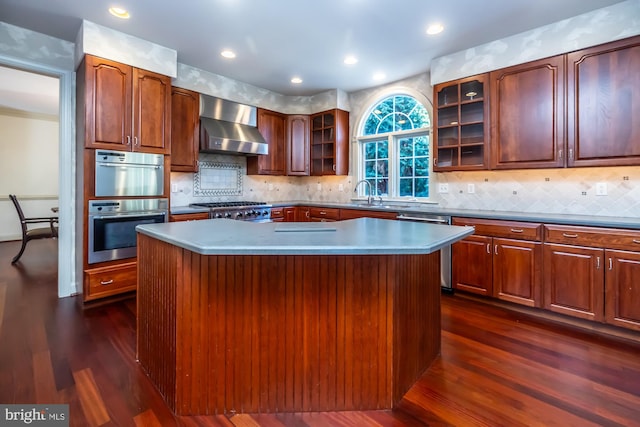 kitchen with dark hardwood / wood-style flooring, stainless steel appliances, a kitchen island, and wall chimney range hood