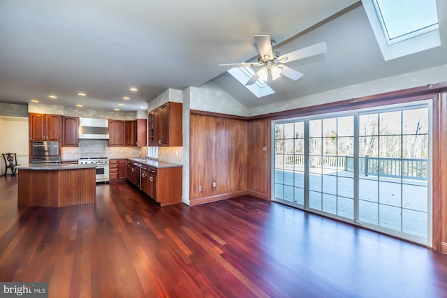 kitchen with a center island, wall chimney exhaust hood, dark wood-type flooring, stainless steel appliances, and vaulted ceiling with skylight