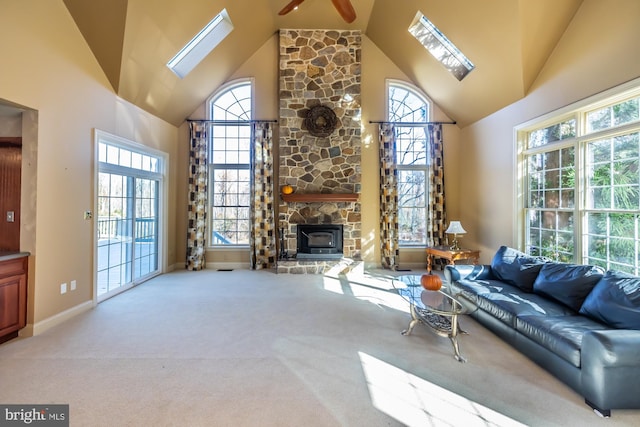 carpeted living room featuring ceiling fan, a stone fireplace, high vaulted ceiling, and a skylight