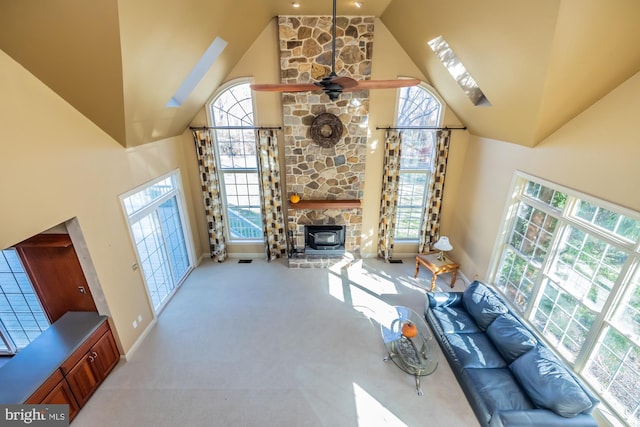 carpeted living room with plenty of natural light, ceiling fan, a stone fireplace, and high vaulted ceiling