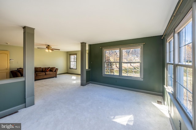 unfurnished living room featuring ornate columns, ceiling fan, and light colored carpet