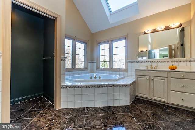 bathroom featuring vanity, a skylight, high vaulted ceiling, and tiled tub