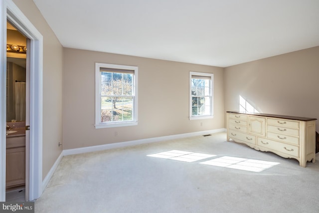 unfurnished bedroom featuring light colored carpet, connected bathroom, and multiple windows