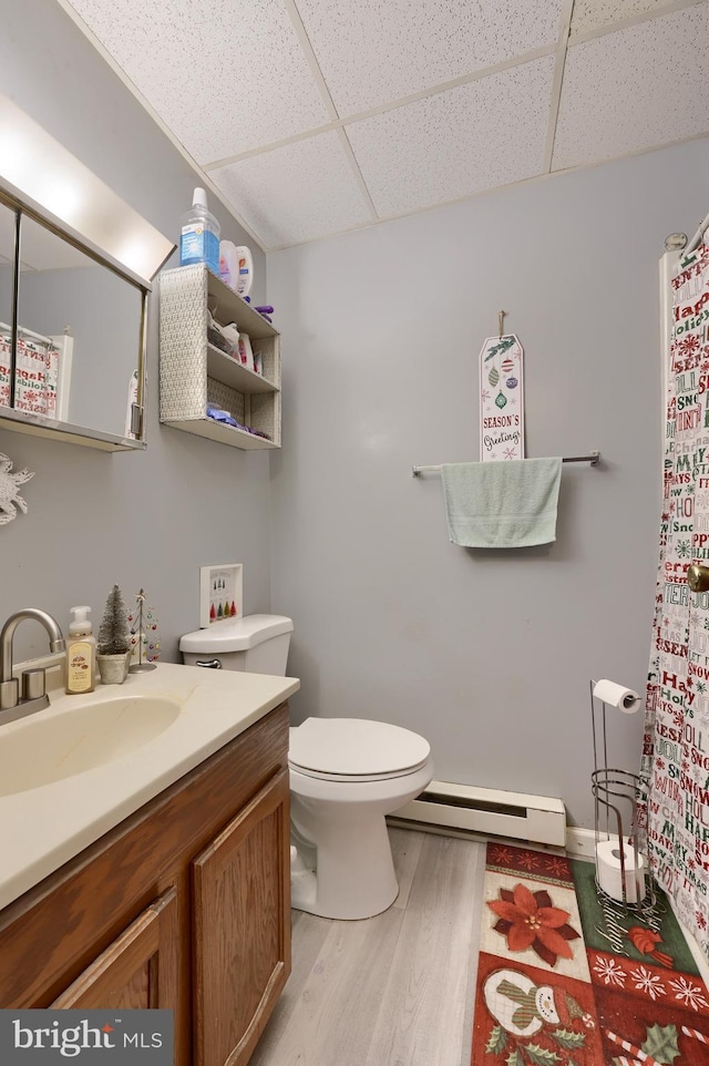 bathroom with vanity, a drop ceiling, hardwood / wood-style flooring, toilet, and a baseboard radiator