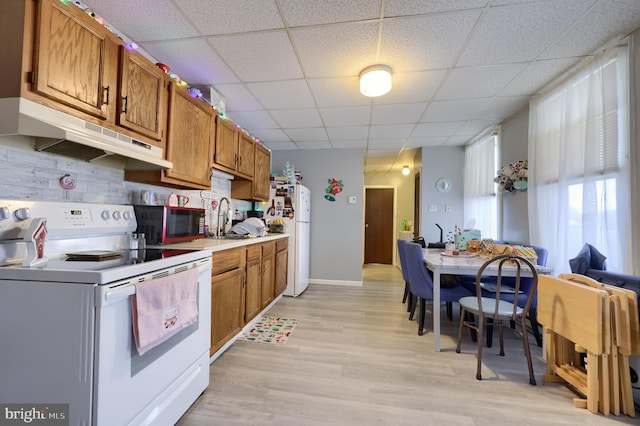 kitchen with a paneled ceiling, white appliances, sink, light hardwood / wood-style flooring, and decorative backsplash