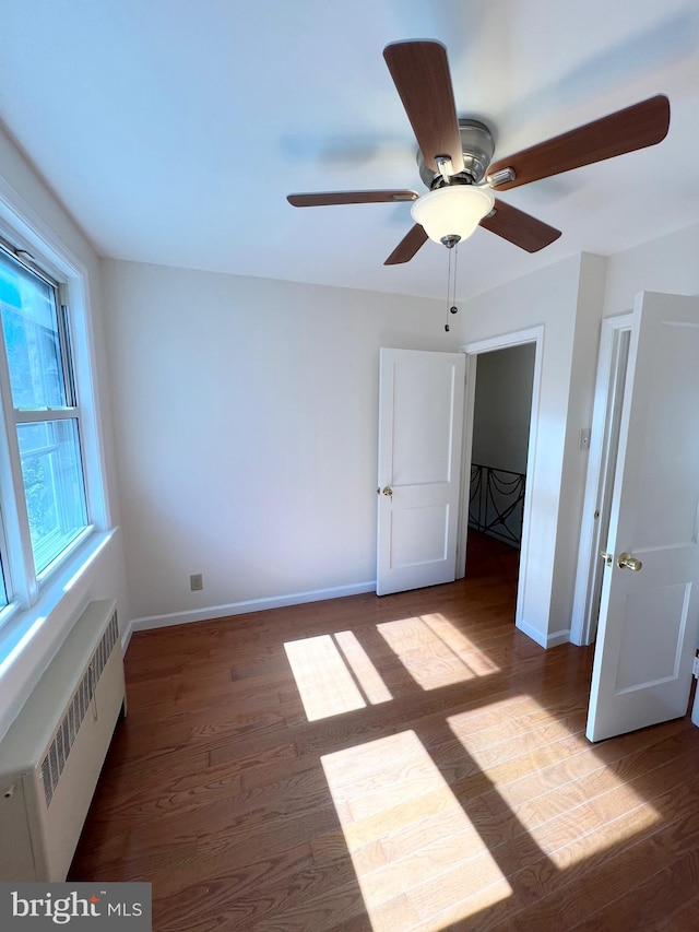 unfurnished bedroom featuring radiator heating unit, dark hardwood / wood-style floors, a spacious closet, and ceiling fan