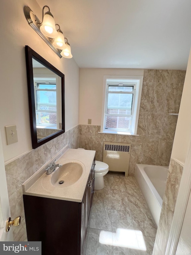 bathroom featuring vanity, tile walls, radiator heating unit, toilet, and a tub