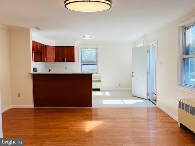 kitchen with kitchen peninsula, radiator heating unit, light wood-type flooring, and crown molding