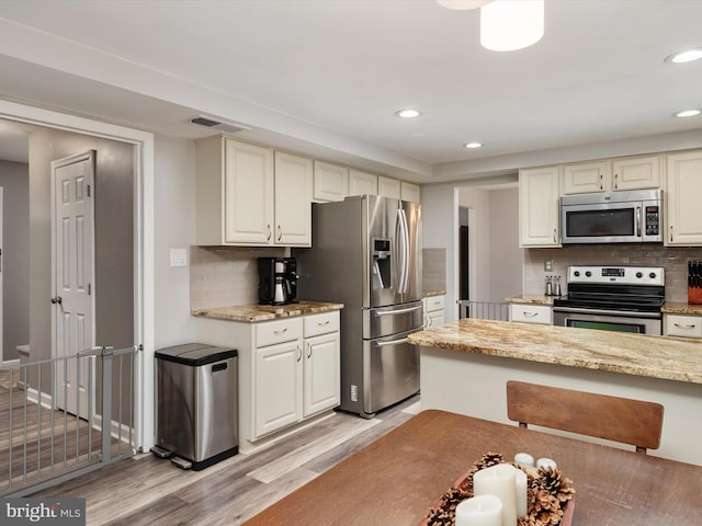 kitchen featuring backsplash, light stone counters, light wood-type flooring, and appliances with stainless steel finishes